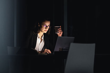 woman in dark room on laptop holding coffee