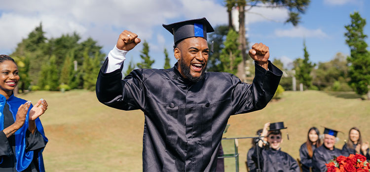A man in a cap and gown celebrates as he graduates