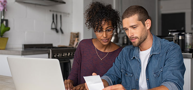 a man and woman review information on a laptop while sitting in their kitchen