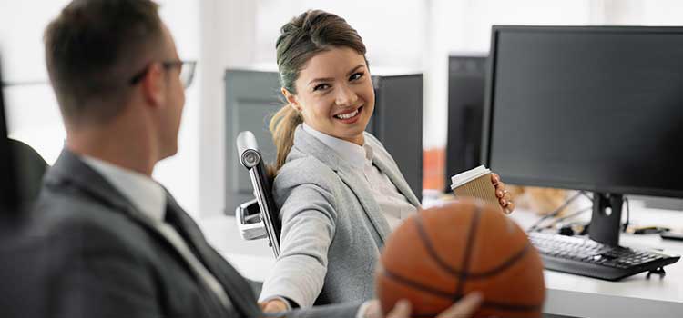 woman at desk smiling at man seated nearby holding basketball
