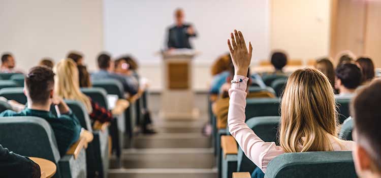 woman in foreground raising hand in auditorium classroom